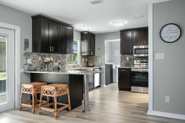 kitchen featuring light stone counters, appliances with stainless steel finishes, a kitchen breakfast bar, and light wood-type flooring