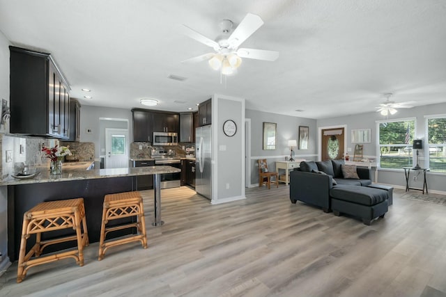 kitchen with appliances with stainless steel finishes, backsplash, a kitchen breakfast bar, light stone countertops, and kitchen peninsula