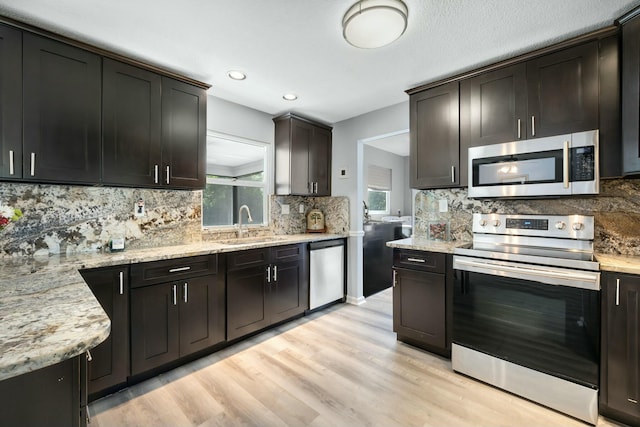 kitchen featuring sink, light stone counters, stainless steel appliances, dark brown cabinets, and light hardwood / wood-style flooring