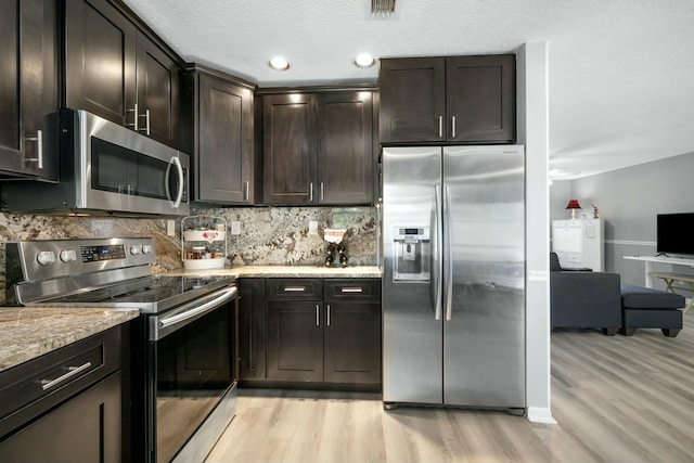 kitchen featuring appliances with stainless steel finishes, tasteful backsplash, light stone counters, dark brown cabinetry, and light hardwood / wood-style flooring