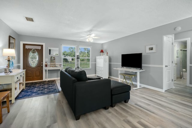 living room with ceiling fan, a textured ceiling, and light wood-type flooring