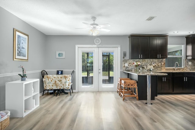 kitchen with tasteful backsplash, dark brown cabinets, light stone countertops, and french doors