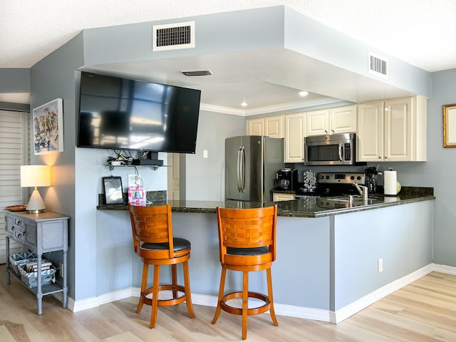 kitchen featuring crown molding, light hardwood / wood-style flooring, dark stone countertops, appliances with stainless steel finishes, and kitchen peninsula