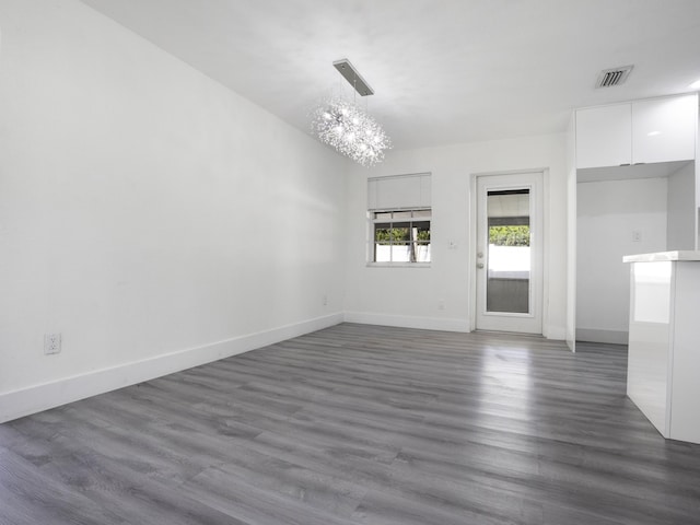 unfurnished room with an inviting chandelier and dark hardwood / wood-style flooring