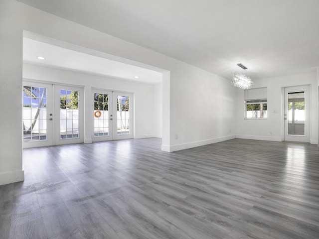 unfurnished living room featuring an inviting chandelier, hardwood / wood-style floors, and french doors