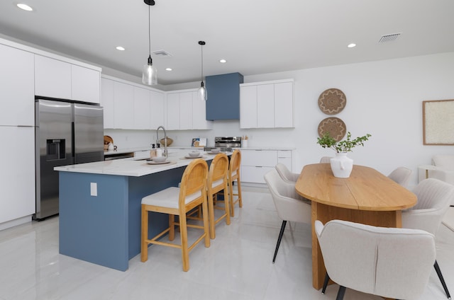 kitchen featuring appliances with stainless steel finishes, a kitchen breakfast bar, an island with sink, white cabinets, and decorative light fixtures