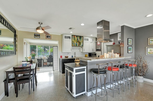 kitchen with a breakfast bar, white cabinetry, crown molding, island range hood, and a center island