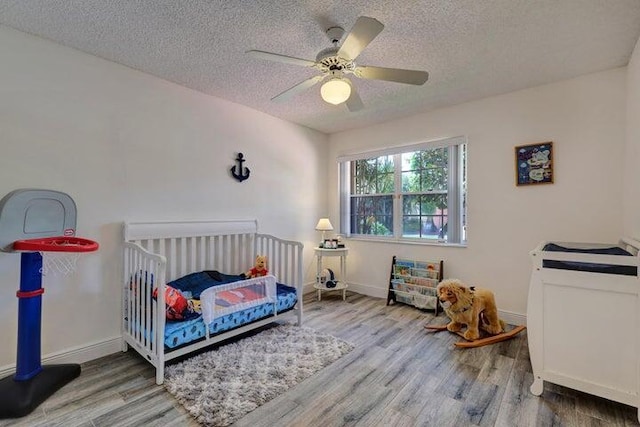 bedroom with a textured ceiling, light hardwood / wood-style flooring, a nursery area, and ceiling fan