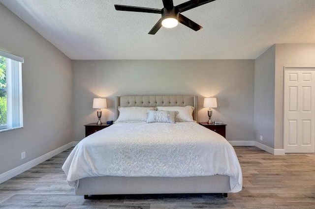 bedroom featuring ceiling fan, light wood-type flooring, multiple windows, and a textured ceiling