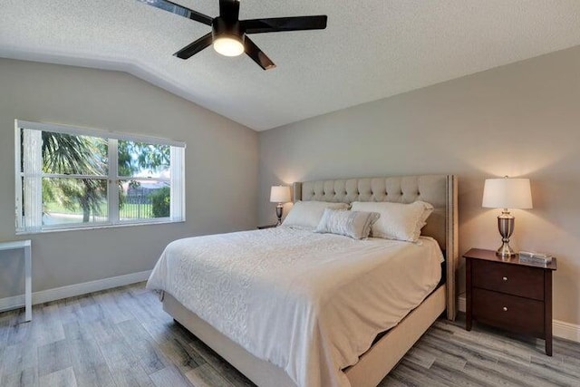 bedroom with lofted ceiling, hardwood / wood-style floors, a textured ceiling, and ceiling fan