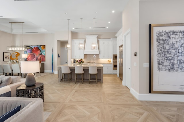 kitchen with a breakfast bar, decorative light fixtures, an island with sink, custom range hood, and white cabinets