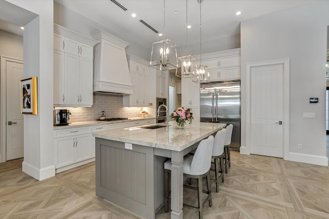 kitchen with stainless steel appliances, an island with sink, white cabinetry, and wall chimney exhaust hood