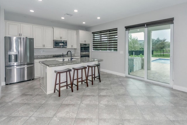 kitchen with white cabinetry, appliances with stainless steel finishes, an island with sink, and stone counters