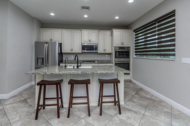 kitchen with sink, white cabinetry, appliances with stainless steel finishes, light stone countertops, and a kitchen island with sink