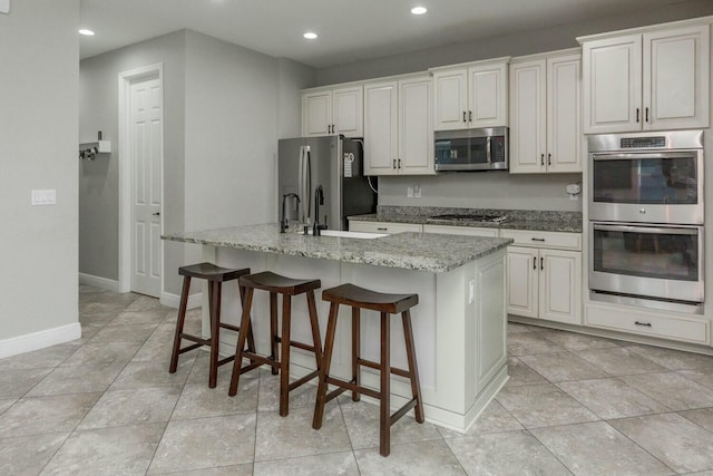 kitchen featuring white cabinetry, a breakfast bar area, a kitchen island with sink, light stone counters, and stainless steel appliances