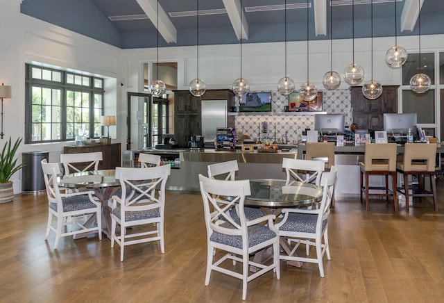 dining area with beam ceiling, hardwood / wood-style flooring, and a high ceiling