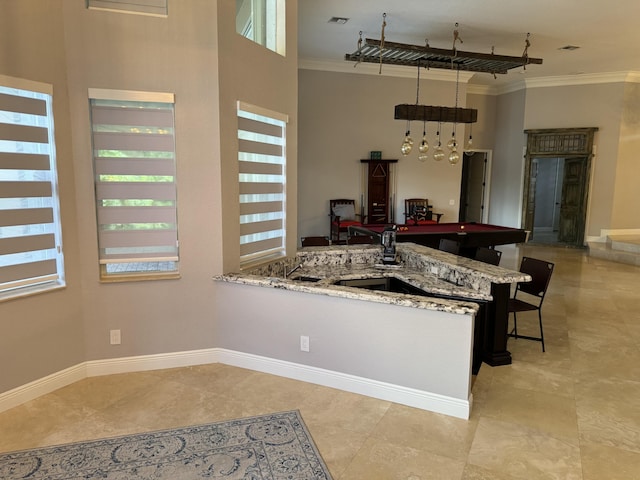 kitchen with a towering ceiling, ornamental molding, light stone countertops, a kitchen bar, and kitchen peninsula