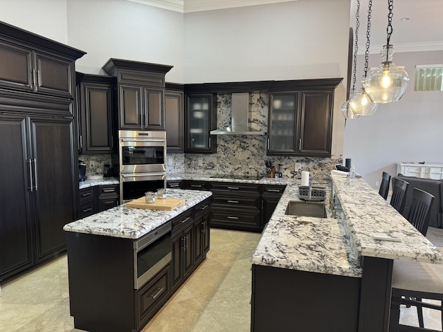 kitchen featuring a kitchen breakfast bar, hanging light fixtures, built in appliances, kitchen peninsula, and wall chimney range hood