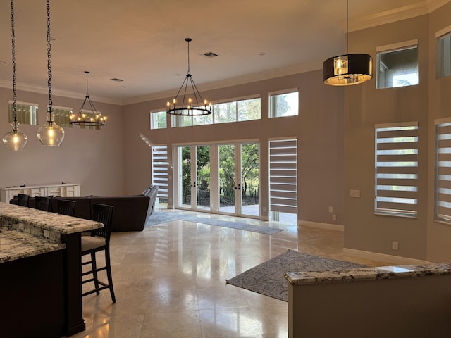 kitchen featuring light stone counters, pendant lighting, ornamental molding, and a towering ceiling