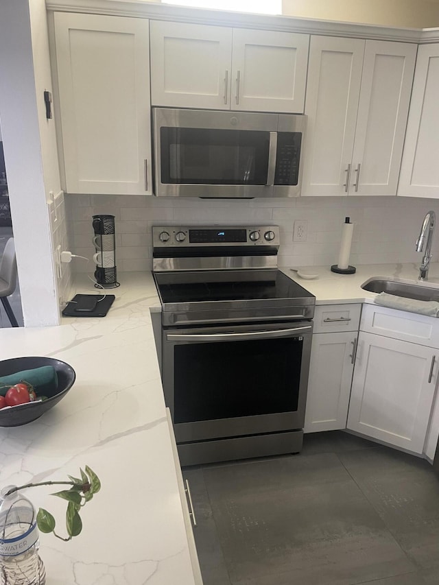 kitchen featuring appliances with stainless steel finishes, white cabinetry, sink, backsplash, and light stone counters