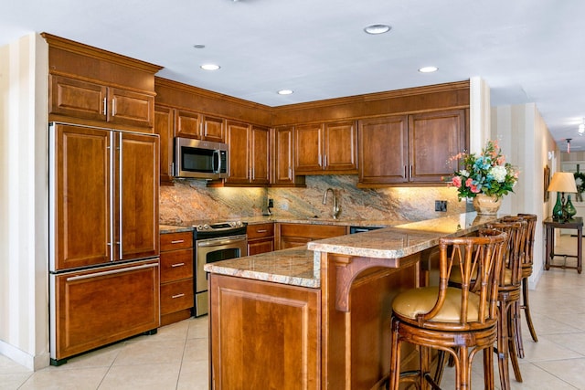 kitchen featuring stainless steel appliances, light tile patterned floors, a kitchen breakfast bar, and kitchen peninsula