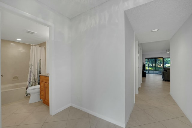 hall with a textured ceiling and light tile patterned floors