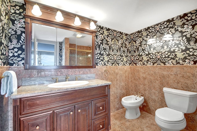 full bathroom with a wainscoted wall, toilet, vanity, and a bidet