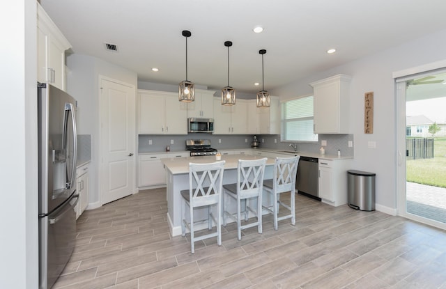 kitchen with a kitchen bar, a center island, appliances with stainless steel finishes, pendant lighting, and white cabinets