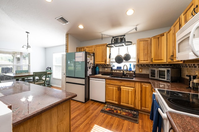 kitchen featuring sink, decorative backsplash, hanging light fixtures, white appliances, and light hardwood / wood-style flooring