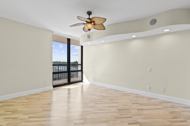 empty room featuring light hardwood / wood-style flooring, a wall of windows, and ceiling fan