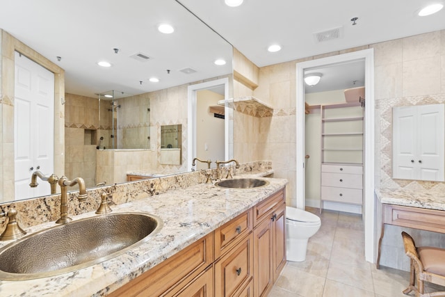 bathroom with a tile shower, tile walls, vanity, toilet, and tile patterned floors