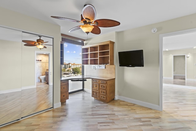 unfurnished office featuring ceiling fan, built in desk, and light wood-type flooring