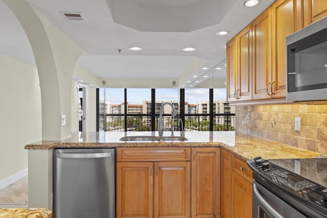 kitchen featuring sink, tasteful backsplash, kitchen peninsula, stainless steel appliances, and light stone countertops