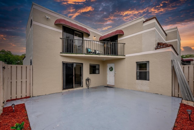 back house at dusk featuring a balcony and a patio area