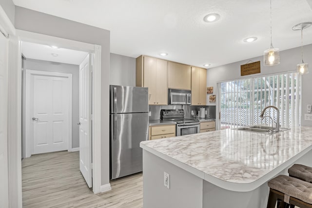 kitchen with decorative light fixtures, sink, a kitchen bar, stainless steel appliances, and light hardwood / wood-style flooring