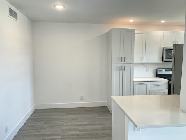 kitchen featuring appliances with stainless steel finishes, backsplash, light hardwood / wood-style floors, white cabinets, and a kitchen bar