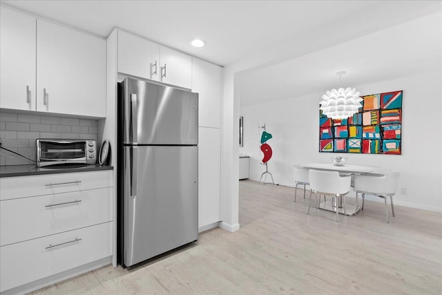 kitchen featuring light wood finished floors, dark countertops, a toaster, freestanding refrigerator, and white cabinets