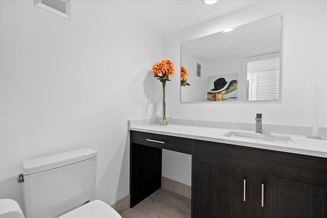 half bathroom featuring visible vents, wood finished floors, vanity, and toilet