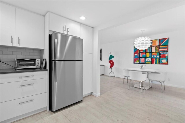 kitchen featuring dark countertops, a toaster, light wood-style flooring, white cabinets, and freestanding refrigerator