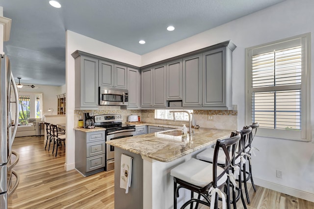 kitchen featuring gray cabinets, sink, light stone counters, kitchen peninsula, and stainless steel appliances