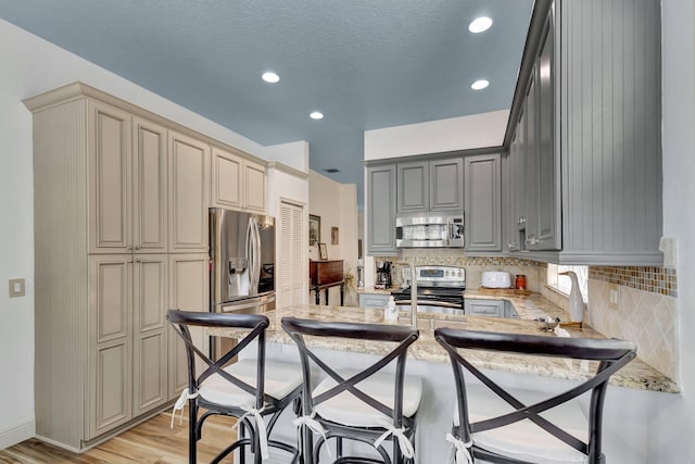 kitchen featuring tasteful backsplash, light hardwood / wood-style flooring, a textured ceiling, appliances with stainless steel finishes, and gray cabinets