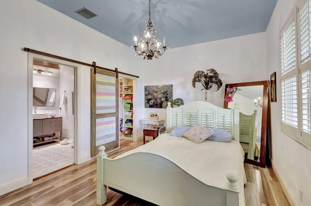 bedroom featuring ensuite bathroom, a barn door, a chandelier, and light hardwood / wood-style flooring