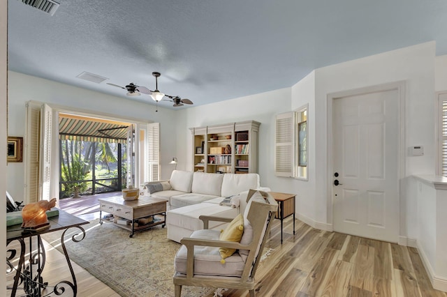 living room featuring ceiling fan, light hardwood / wood-style floors, and a textured ceiling