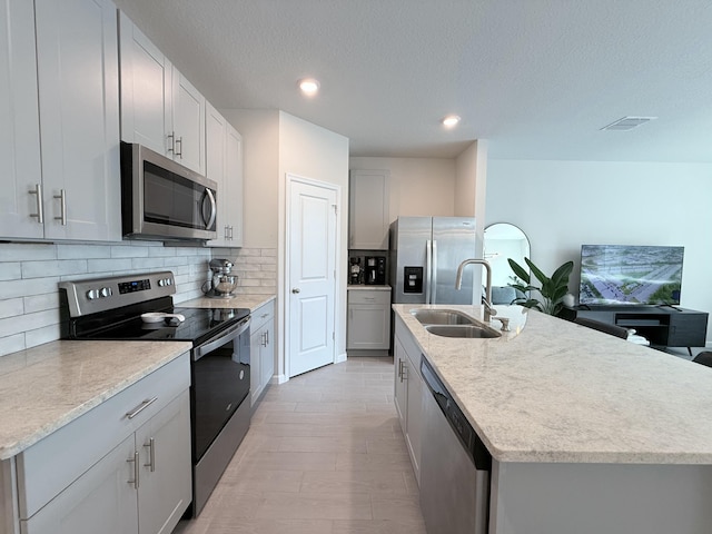 kitchen featuring tasteful backsplash, appliances with stainless steel finishes, a kitchen island with sink, and sink