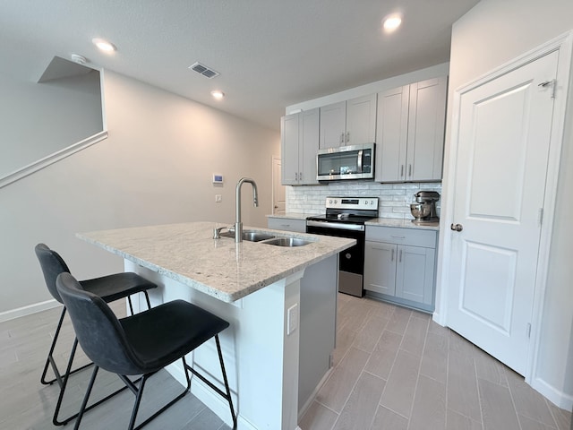 kitchen with sink, gray cabinets, a breakfast bar, stainless steel appliances, and an island with sink