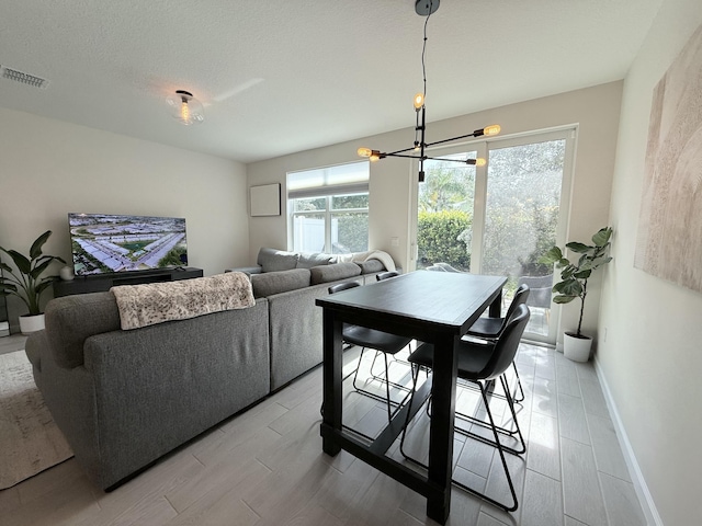 dining space with a chandelier, a wealth of natural light, a textured ceiling, and light hardwood / wood-style floors