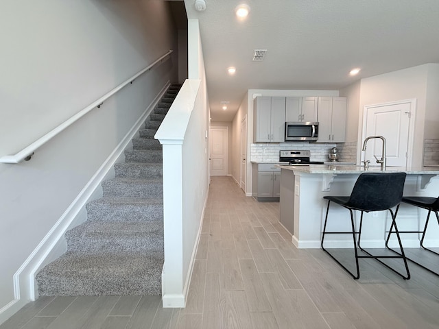 kitchen featuring appliances with stainless steel finishes, tasteful backsplash, gray cabinetry, a kitchen bar, and light stone countertops