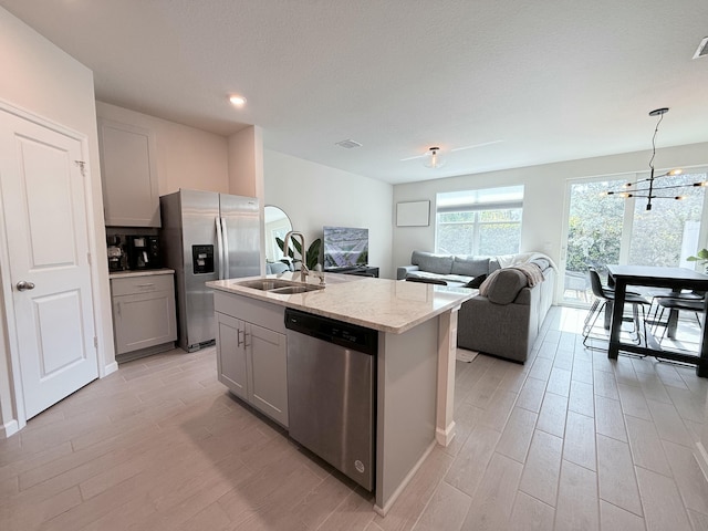 kitchen with appliances with stainless steel finishes, sink, gray cabinetry, hanging light fixtures, and a kitchen island with sink