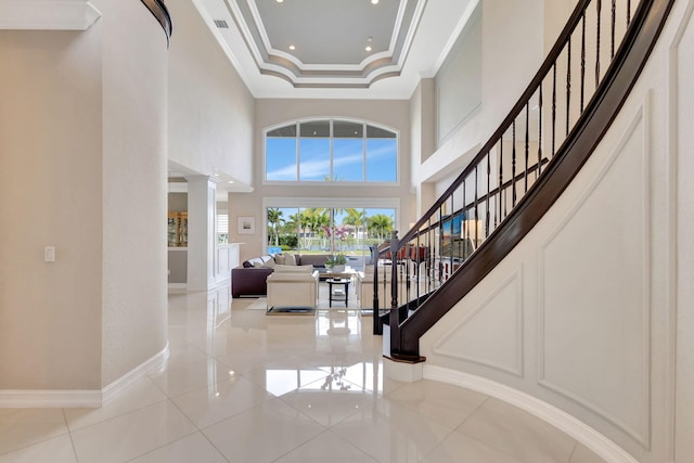 foyer with decorative columns, a high ceiling, ornamental molding, light tile patterned floors, and a raised ceiling