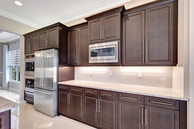 kitchen with dark brown cabinetry, crown molding, stainless steel appliances, light stone countertops, and decorative backsplash